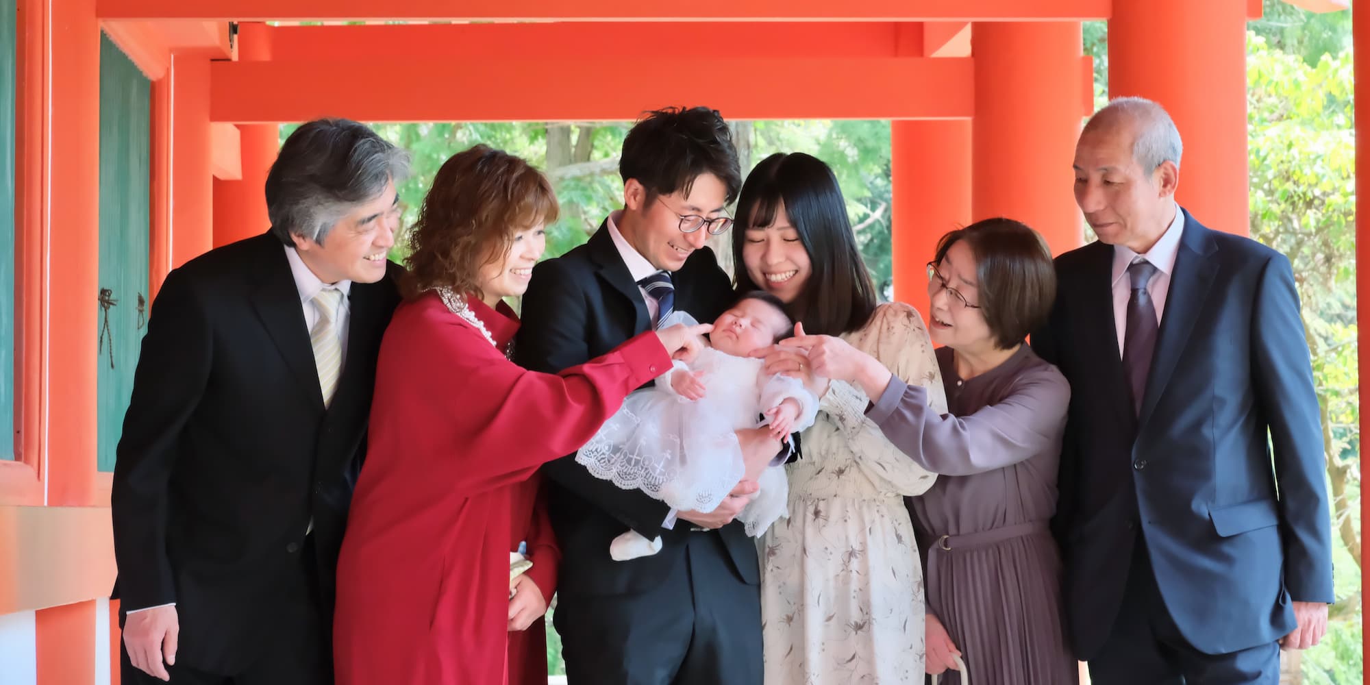 赤い鳥居の下でお宮参りのお祝いをしている家族