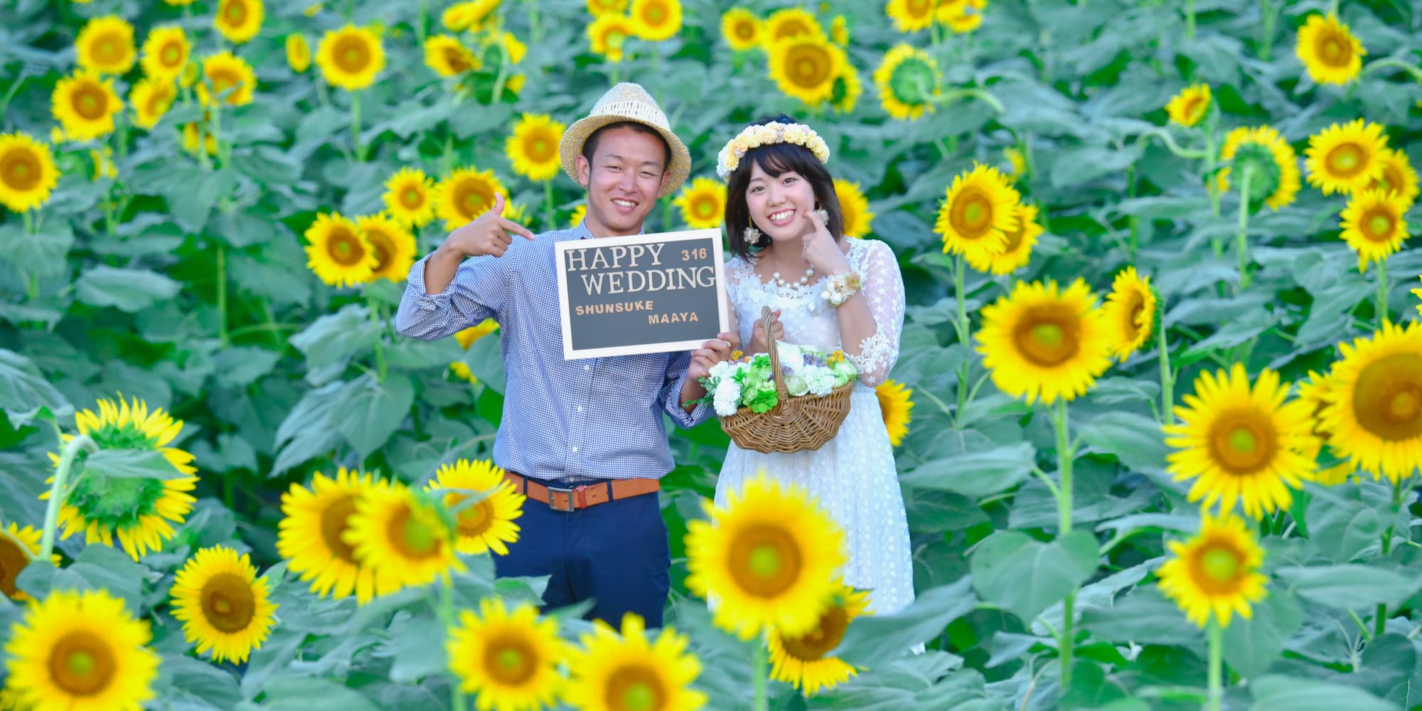 ひまわり畑でウエルカムボードを持ってフォトウェディングを撮影している新郎新婦