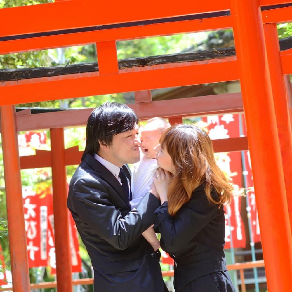 赤い鳥居の前で赤ちゃんを抱っこしているお父さんとお母さん