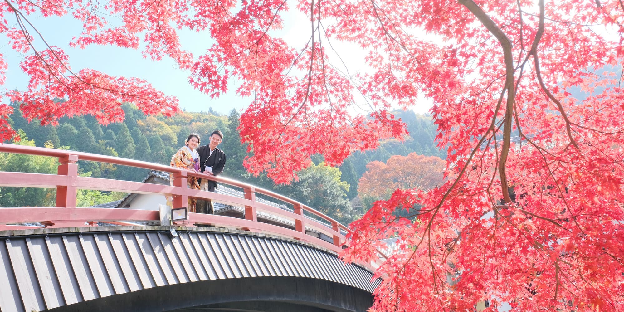 紅葉が美しい橋の上で色打掛を着た花嫁と紋付羽織袴の新郎