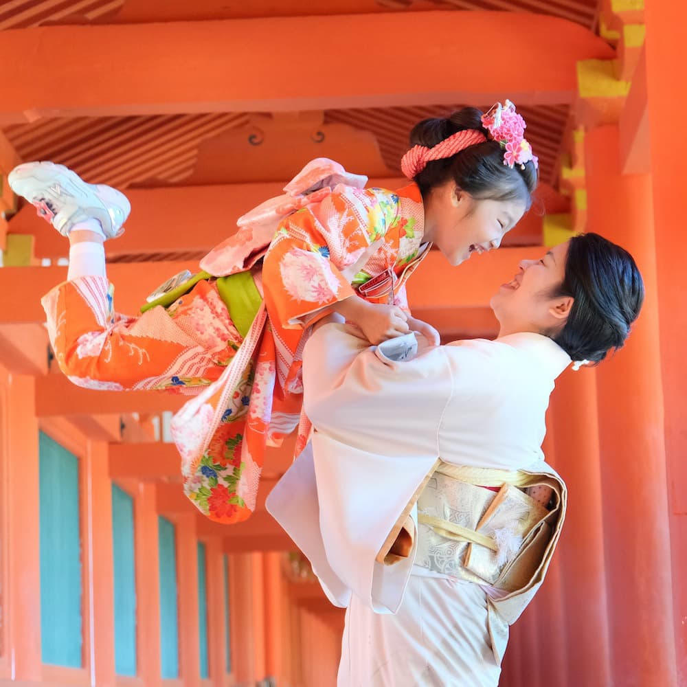 赤い鳥居の前で娘を抱き上げる母親