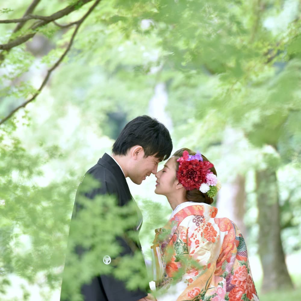 色打掛を着た花嫁様と紋付羽織袴を着た新郎様が顔をくっつけている