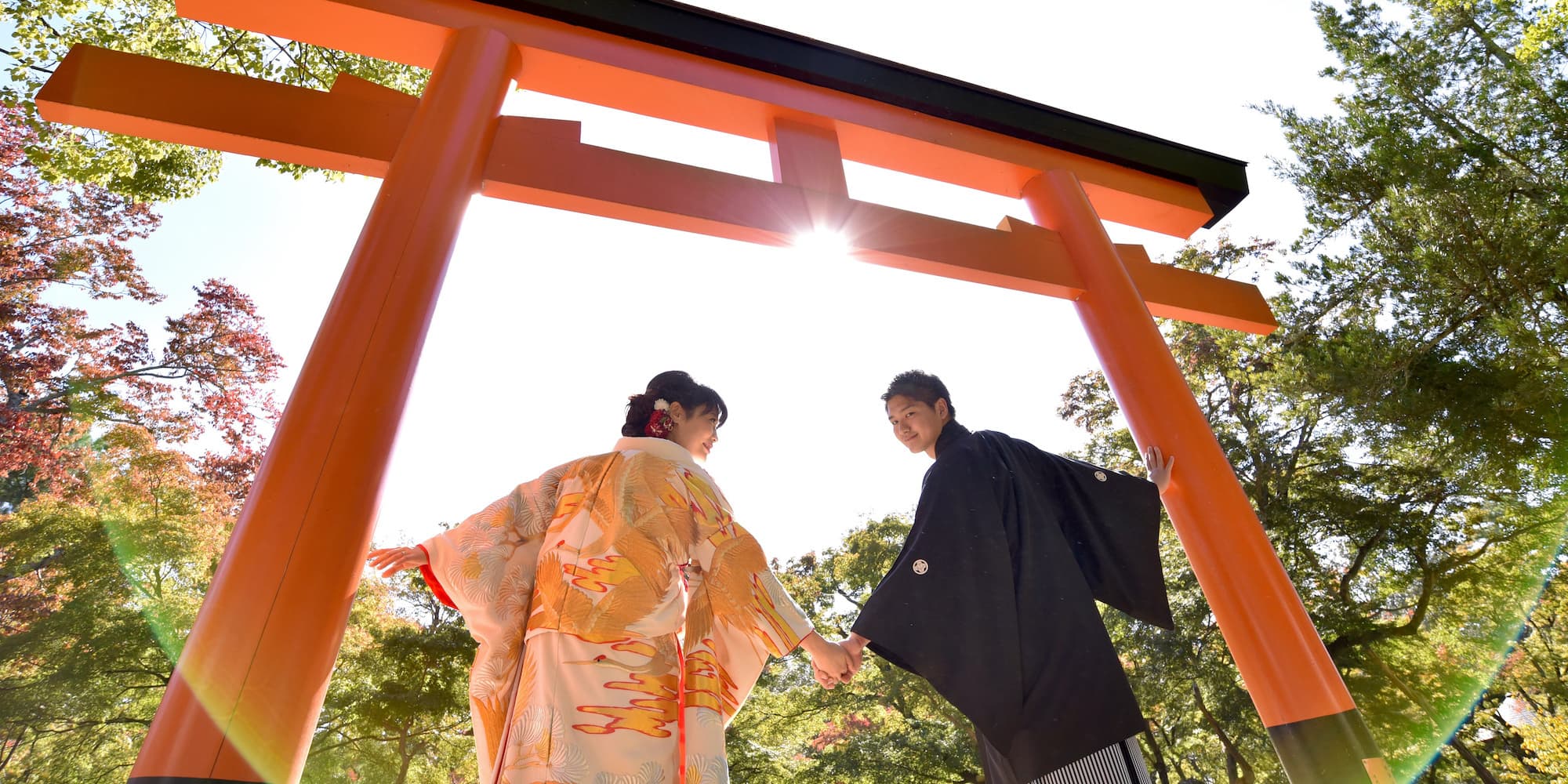 色打掛を着た花嫁様と紋付羽織袴を着た新郎様が鳥居の下で手を繋いでいる