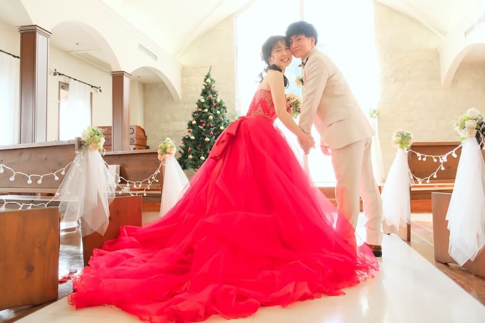 アイドレスと白いタキシードを着て、クリスマスツリーの前で 手をつないで振り返っている新郎新婦