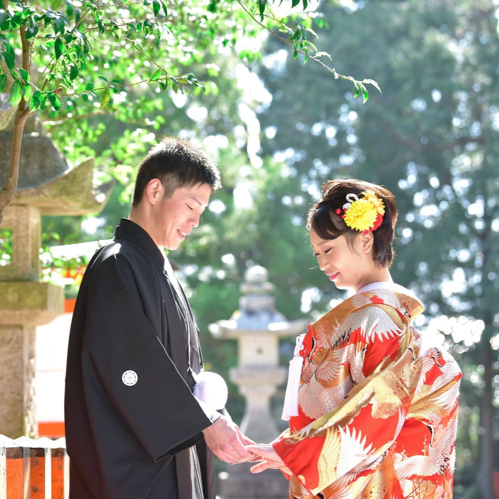 色打掛を着た花嫁様と紋付羽織袴を着た新郎様が神社で結婚式を挙げている