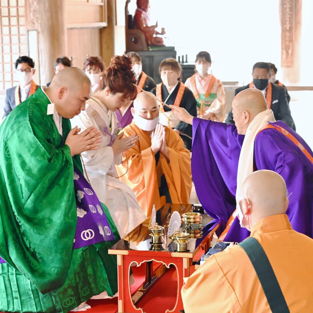 白無垢を着た花嫁様と紋付羽織袴を着た新郎様が寺院で結婚式を挙げている