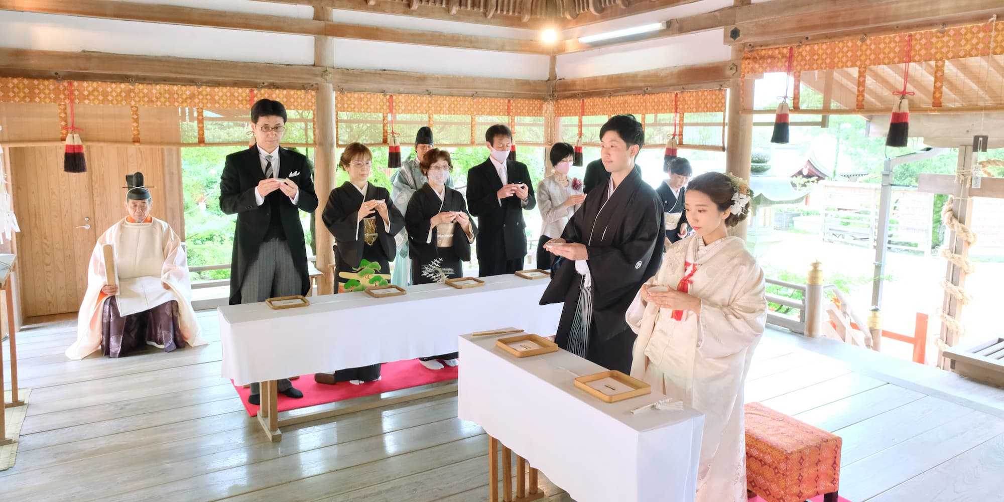 白無垢を着た花嫁様と紋付羽織袴を着た新郎様が神社で結婚式を挙げている