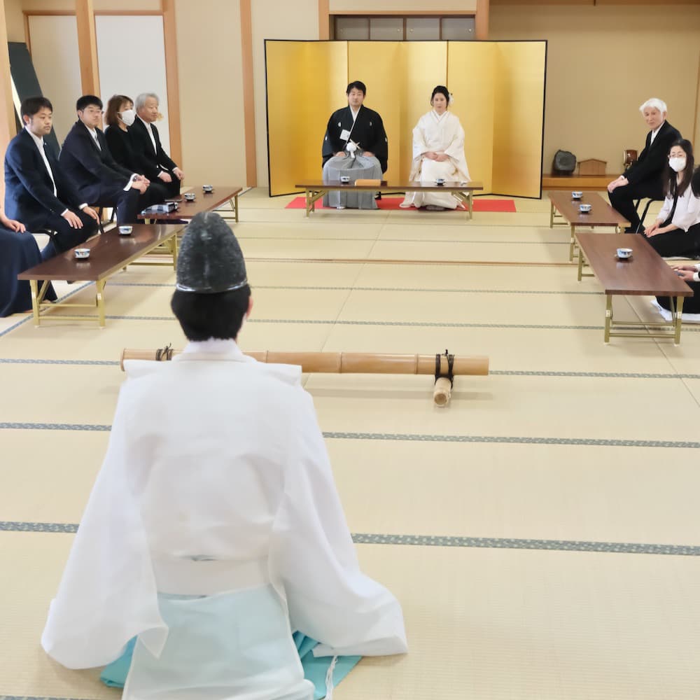 白無垢を着た花嫁様と紋付羽織袴を着た新郎様が神社で結婚式を挙げている