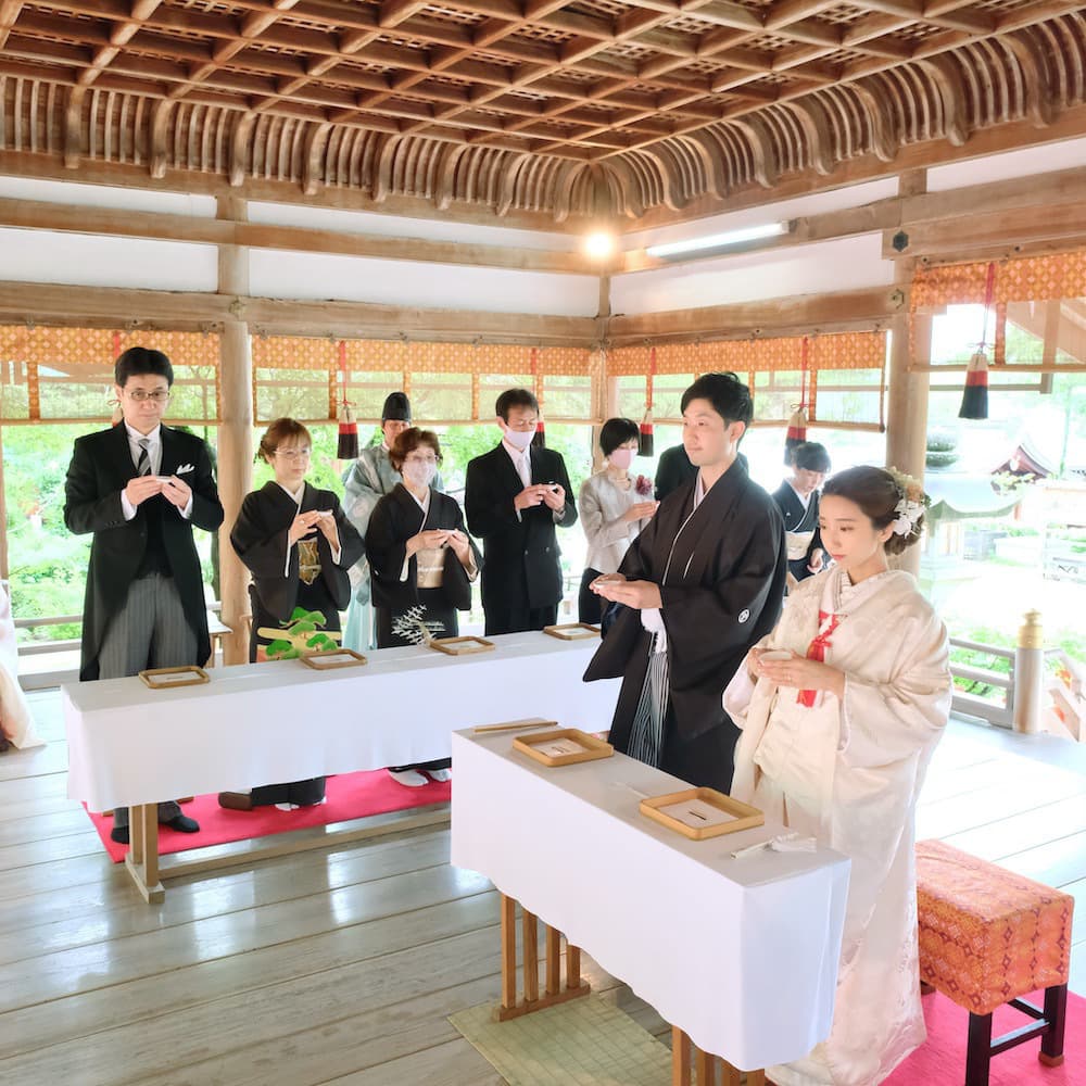 白無垢を着た花嫁様と紋付羽織袴を着た新郎様が神社で結婚式を挙げている