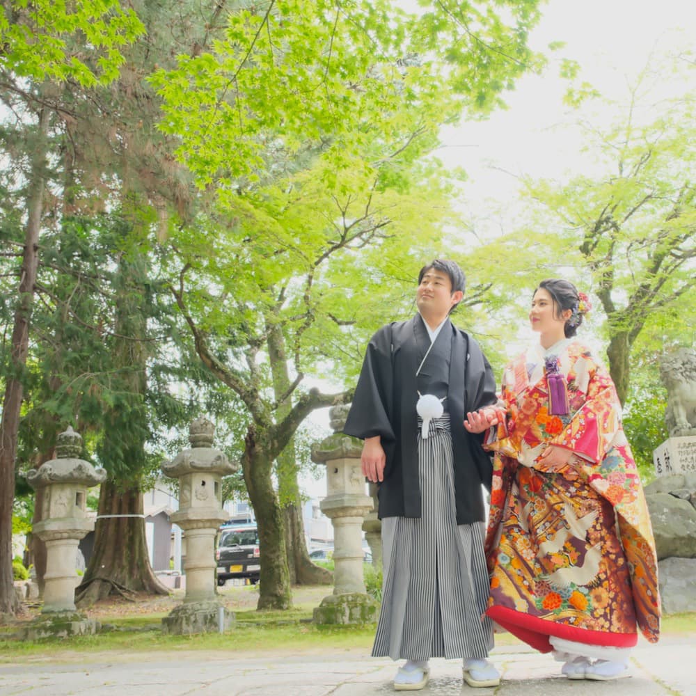 色打掛を着た花嫁様と紋付羽織袴を着た新郎様が神社で結婚式を挙げている