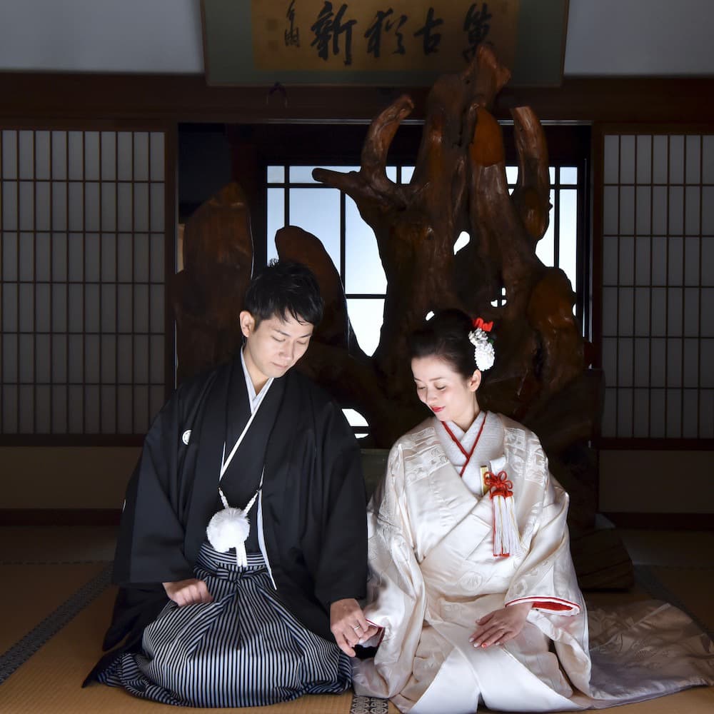 白無垢を着た花嫁様と紋付羽織袴を着た新郎様が神社で結婚式を挙げている