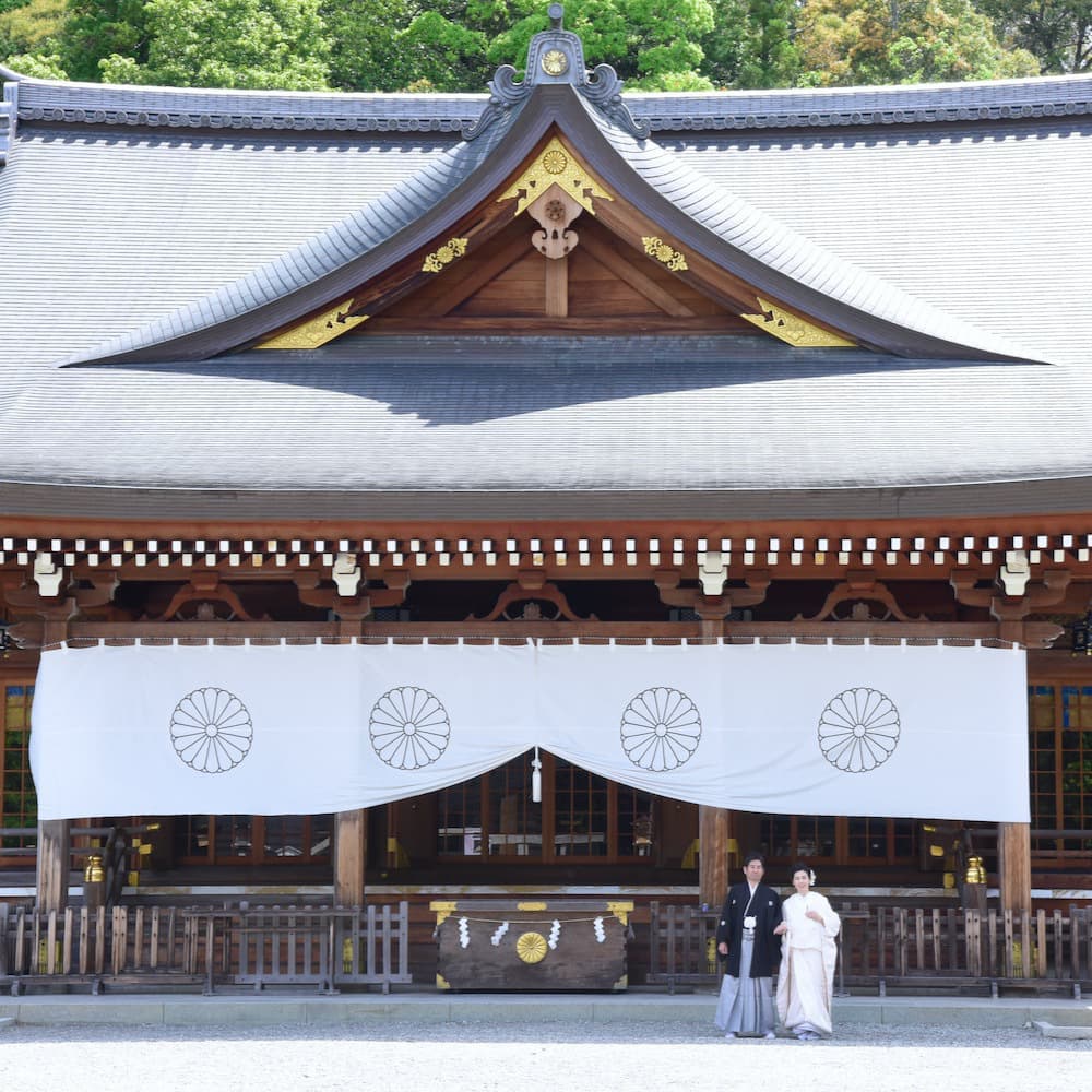 白無垢を着た花嫁様と紋付羽織袴を着た新郎様が神社で結婚式を挙げている