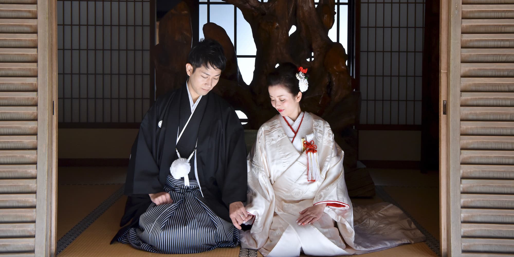 白無垢を着た花嫁様と紋付羽織袴を着た新郎様が神社で結婚式を挙げている