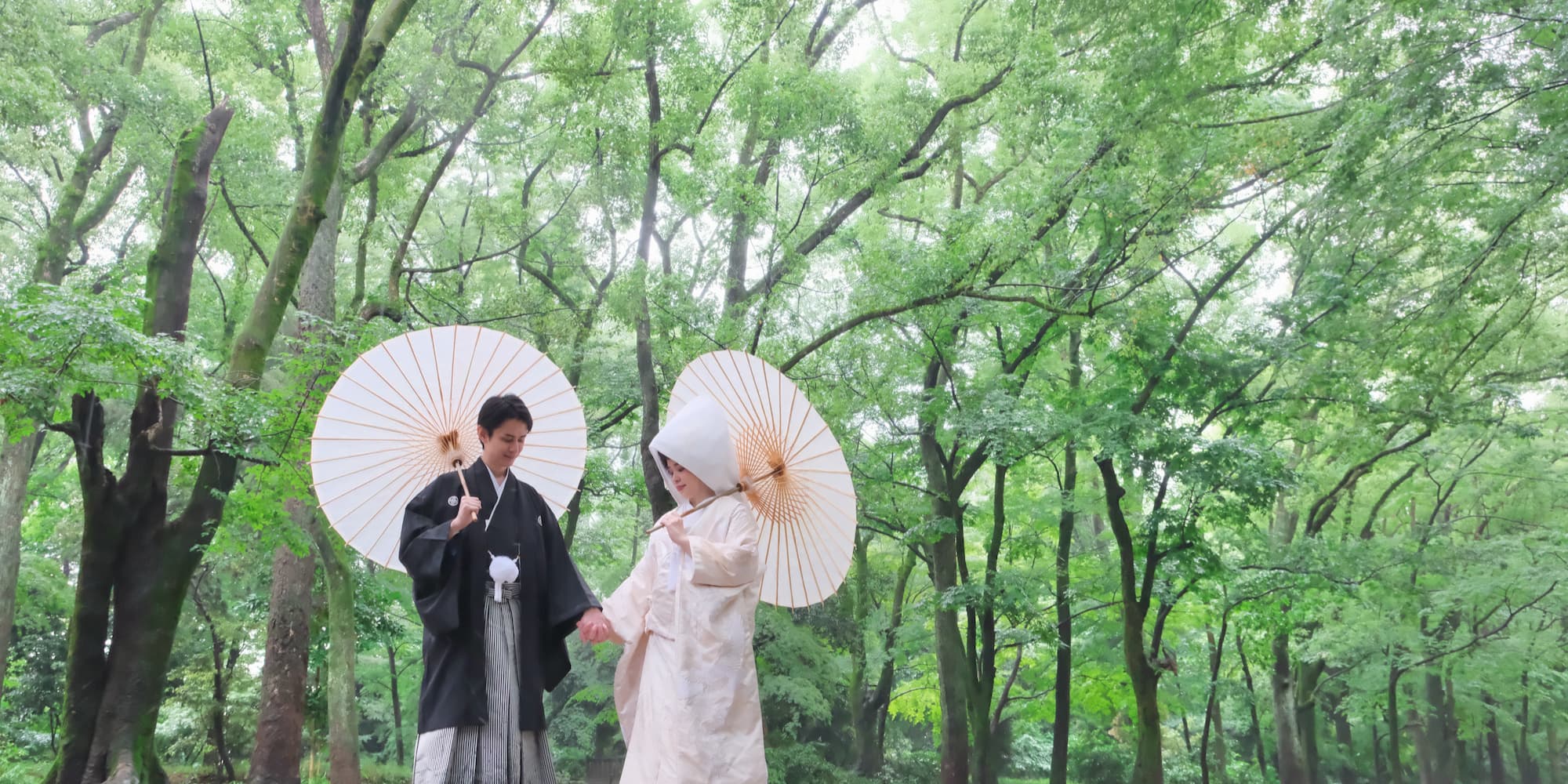 白無垢を着た花嫁様と紋付羽織袴を着た新郎様が番傘をさして手を繋いでいる