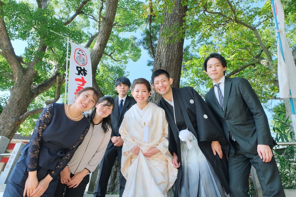 白無垢の花嫁様と紋付羽織袴の新郎様が家族や友人と写真を撮っている