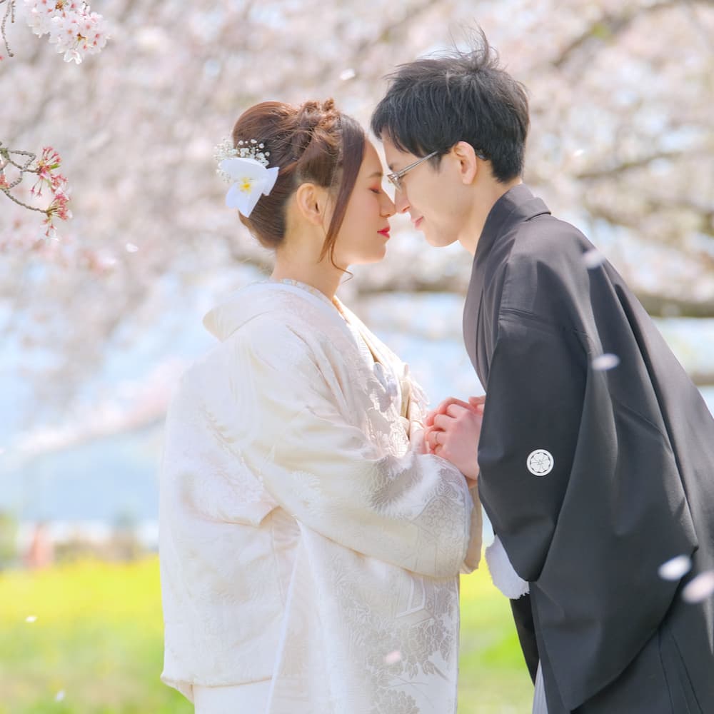 色打掛を着た花嫁様と紋付羽織袴を着た新郎様が神社で結婚式を挙げている