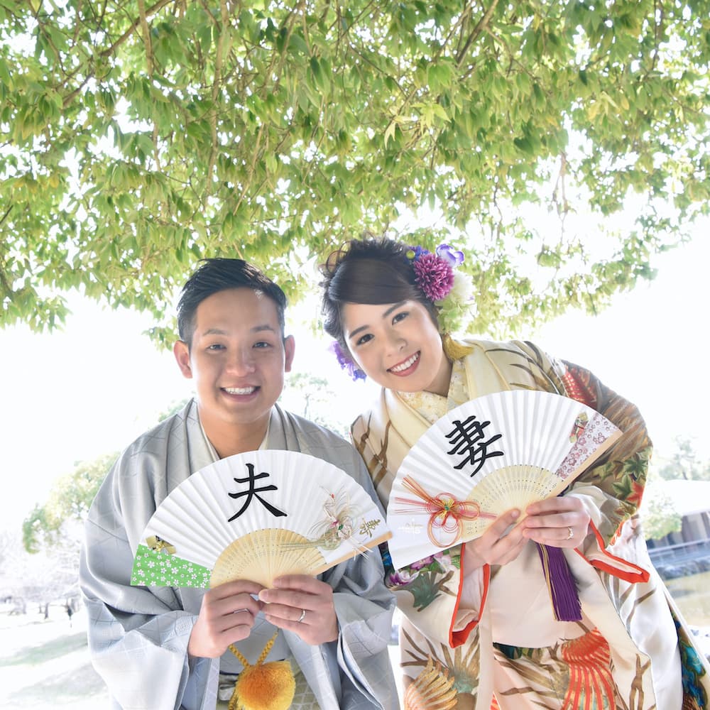 白無垢を着た花嫁様と紋付羽織袴を着た新郎様が神社で手を繋いで歩いている