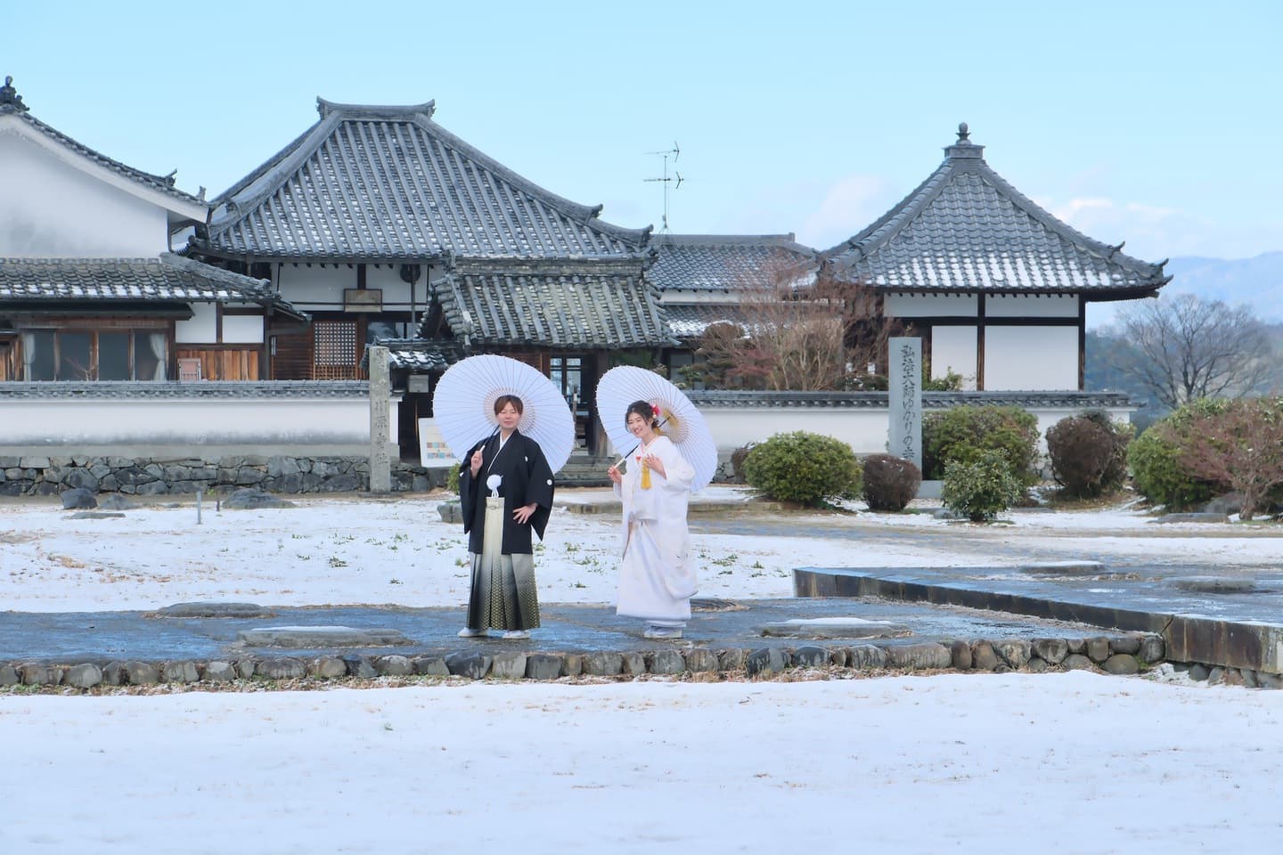 石舞台古墳の雪景色で和傘をさして撮影する白無垢と紋付袴の新郎新婦